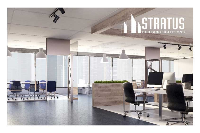 A clean and empty office space with rolling chairs, desks, computers, and large windows.