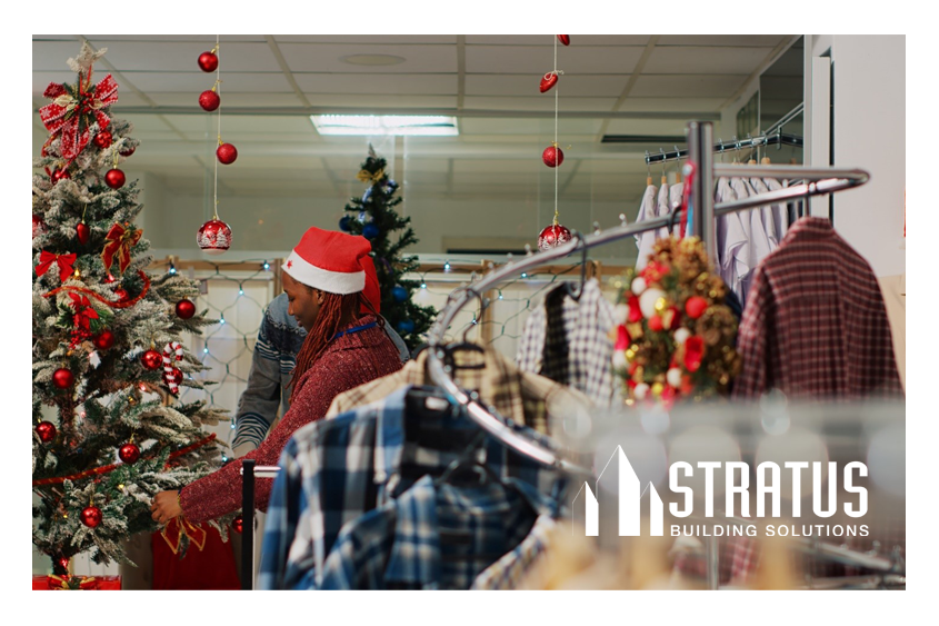 A rack of clothes in front a Christmas tree and a retail worker decorating a store for Christmas.