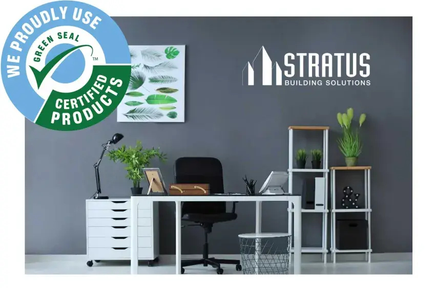 A picture of an office space with white desks, a black rolling chair, and several plants.