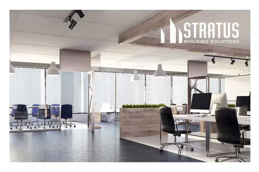 A clean and empty office space with rolling chairs, desks, computers, and large windows.